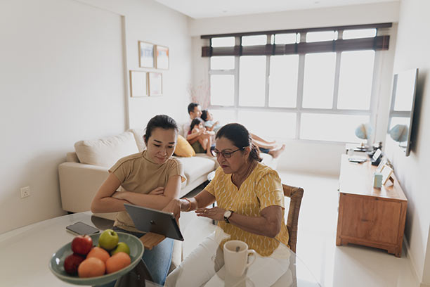 A young woman sits with her mother at their kitchen table to review information on an ipad.