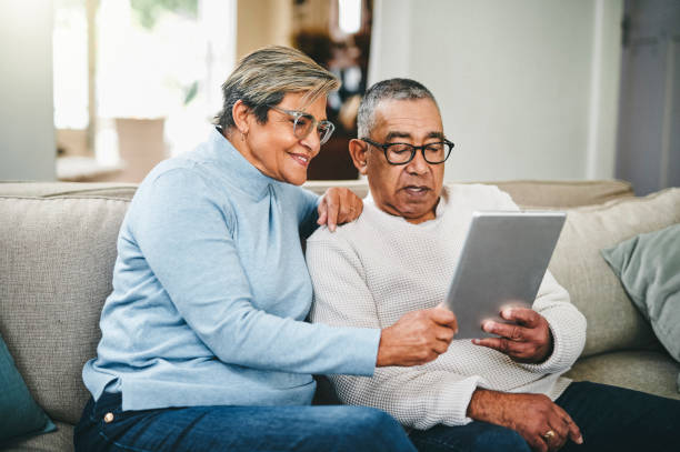 An older couple sit on their couch and look at a tablet together.