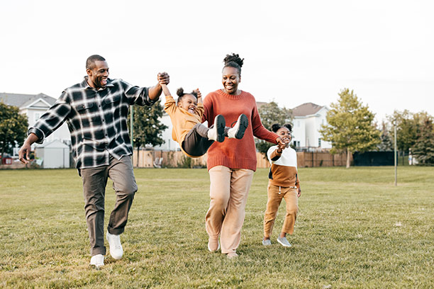 A Black mother and father swing their small child between them and the mother holds her other daughter's hand.