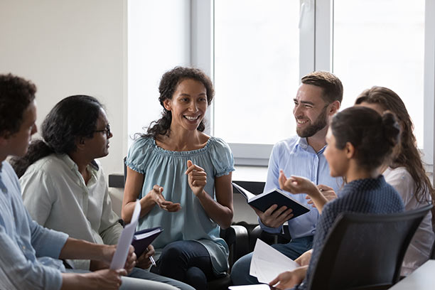 A group of 6 young professionals sit in a circle talking actively.