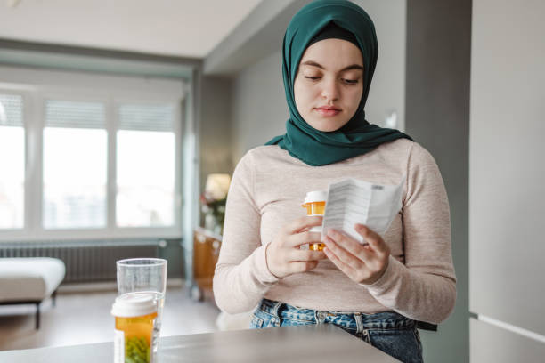 A young woman wearing a green hijab holds a pillbox and reads the informational packet.