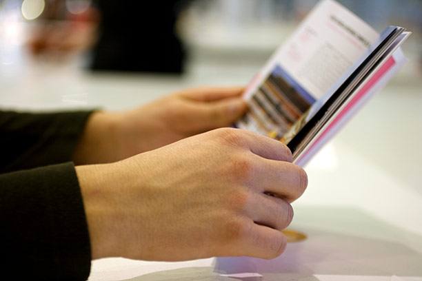 Hands hold open a booklet on a table.