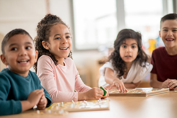 A group of 4 diverse children, around 4 years old, smile and craft at a table.