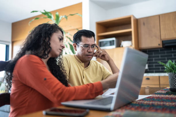 A woman with dark curly hair shows her father something on a laptop screen while sitting at a table.