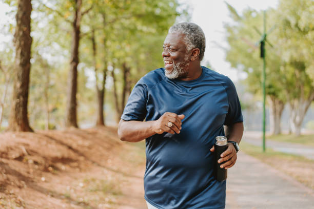 An older Black man smiles while jogging outside on a trail.