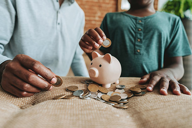 A father and son put coins in a small, pink piggy bank.