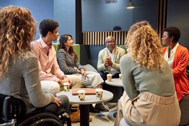 A diverse group of 6 people sit and talk around two small tables at a cafe.