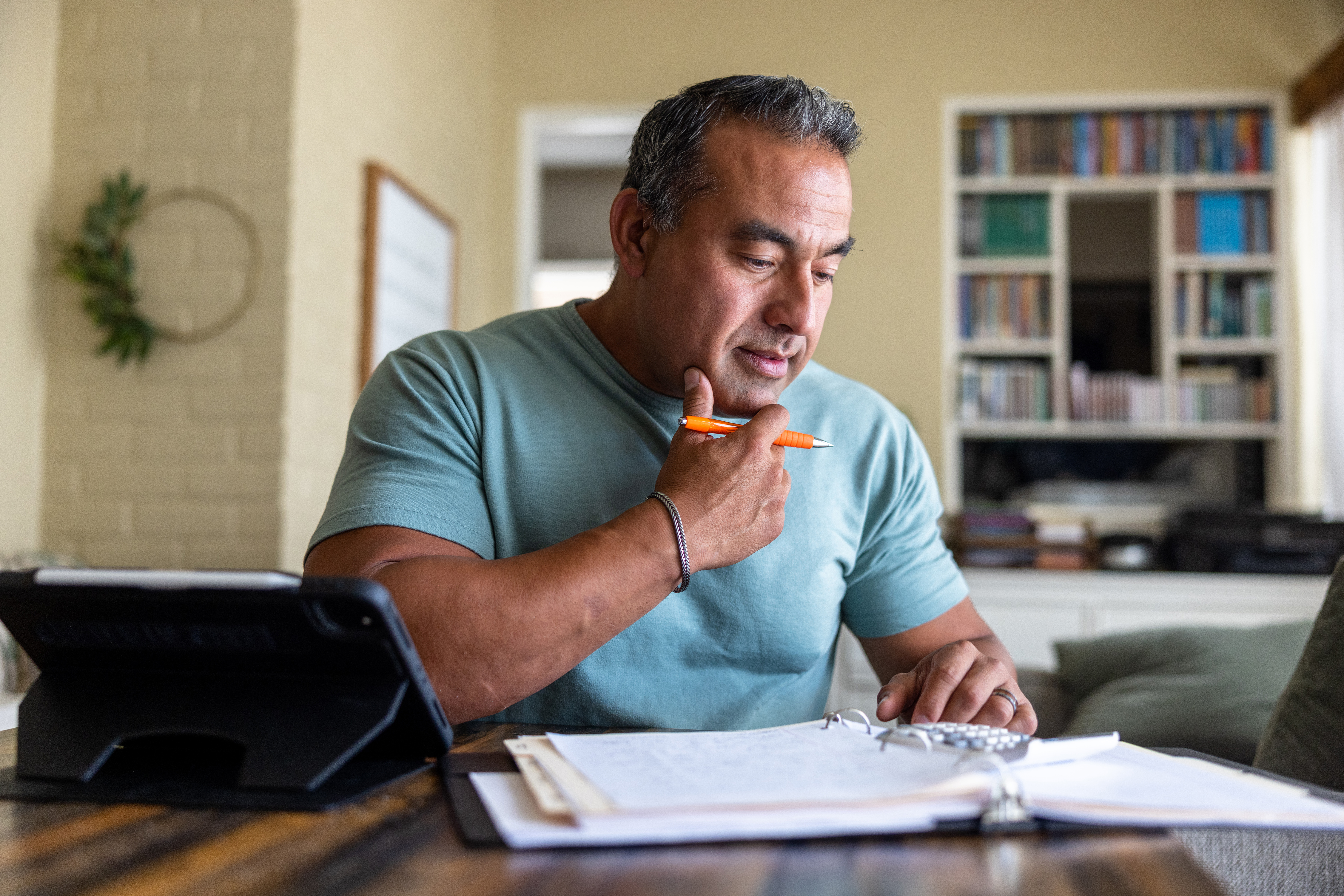 A man sits at a table in his living room and reviews information in a binder.