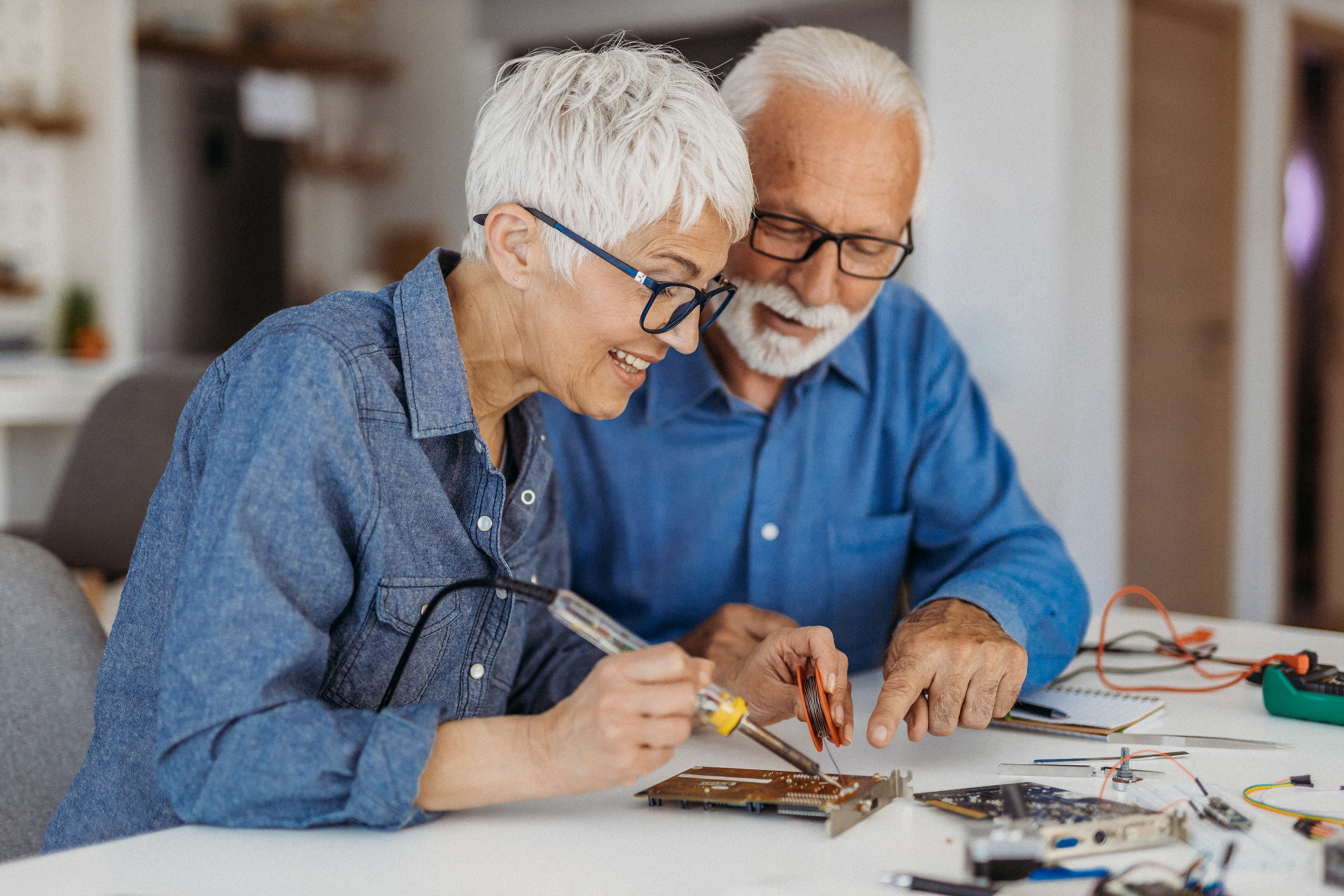 An older man and woman sit at a table and work on a robotics project together.