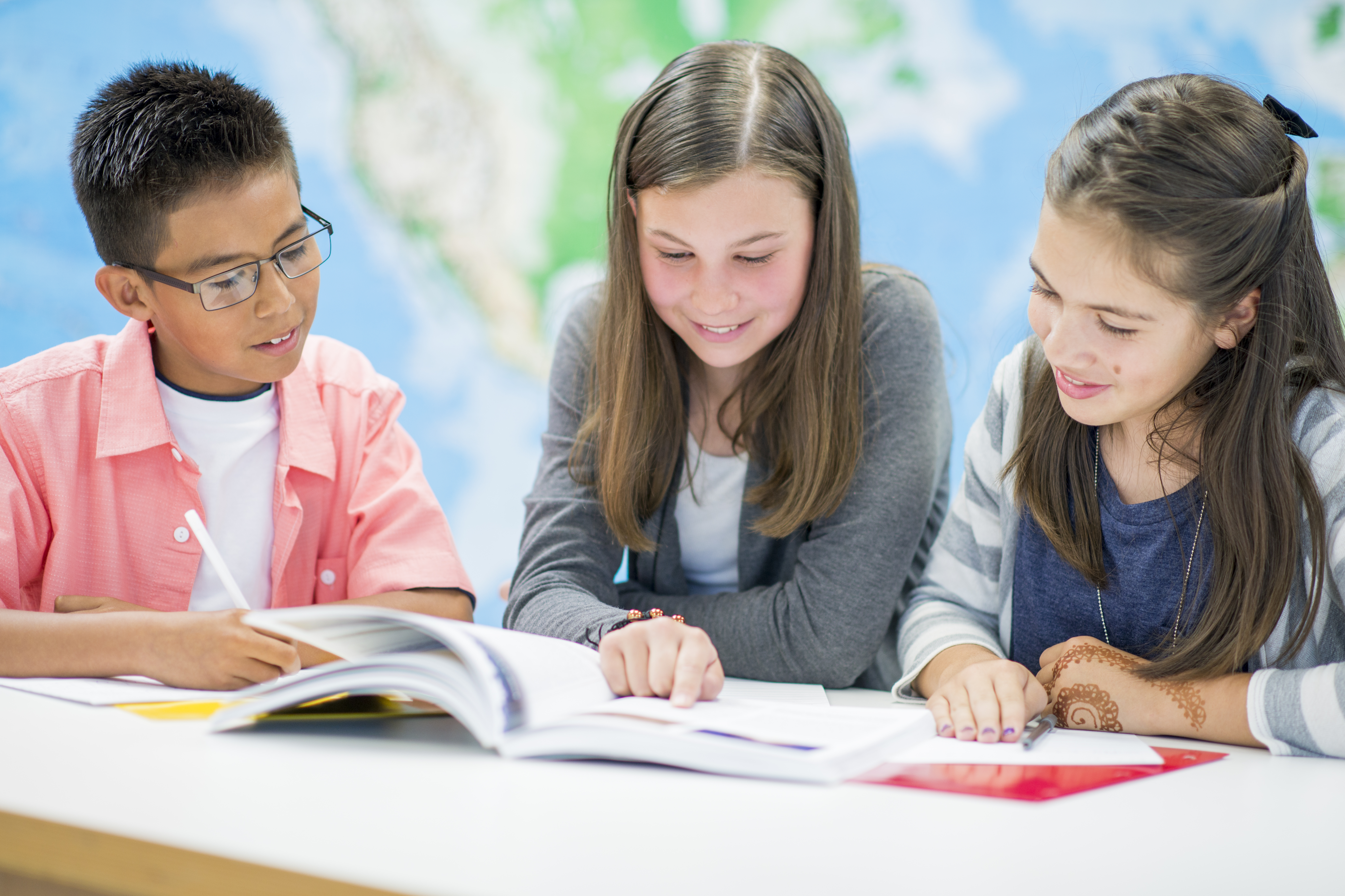 Three elementary school aged children sit together and read a book.