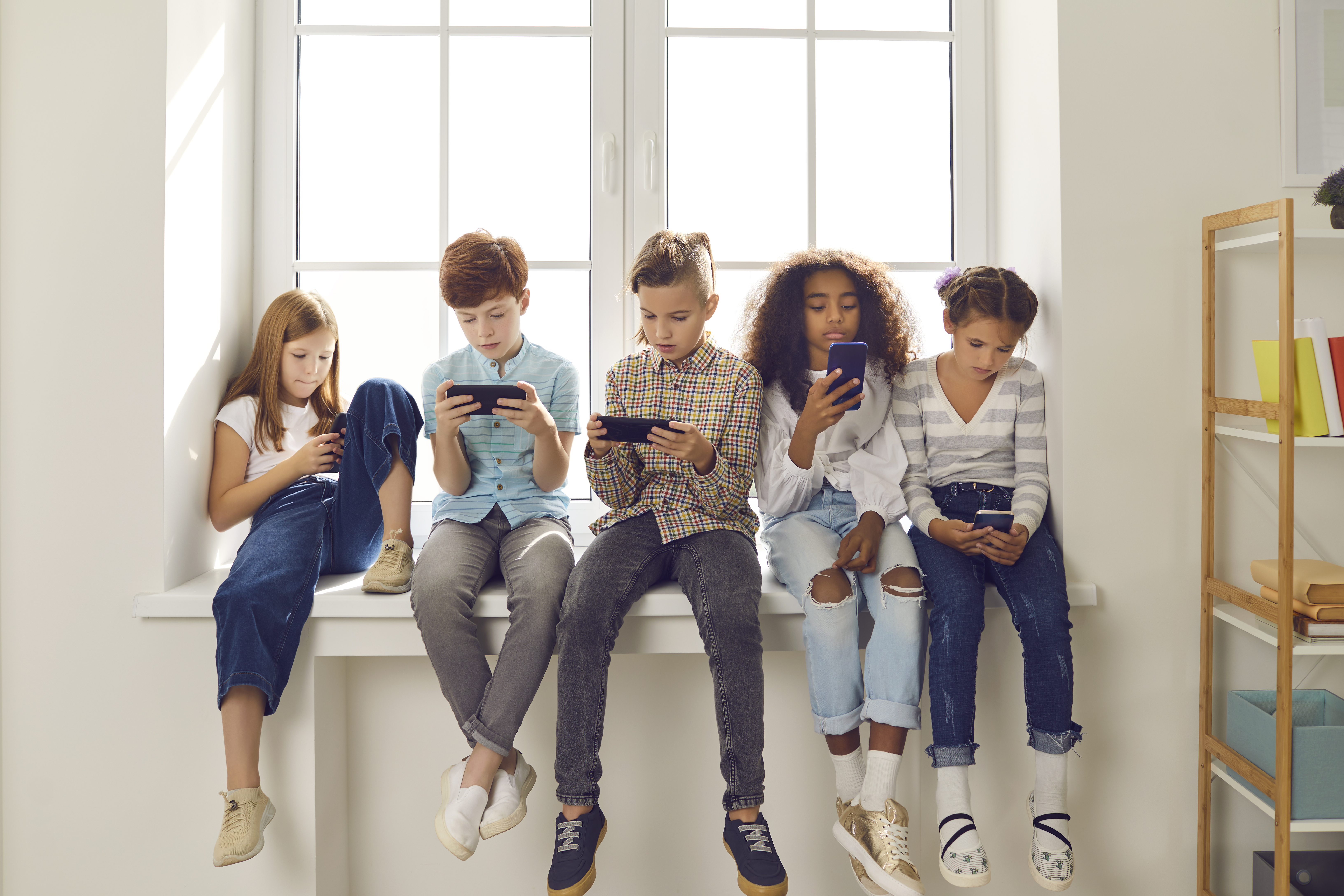 A group of 5 young kids sit along a windowsill.