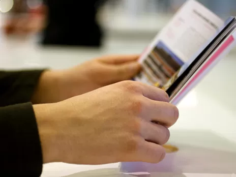 Hands hold open a booklet on a table.