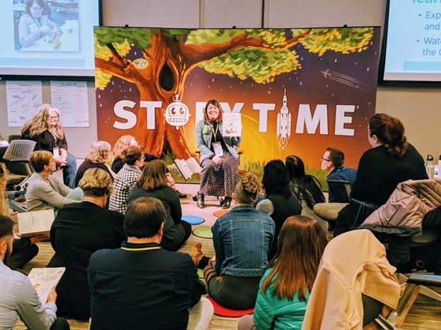 Group of adults sitting, facing a woman reading in front of a large story time poster. 