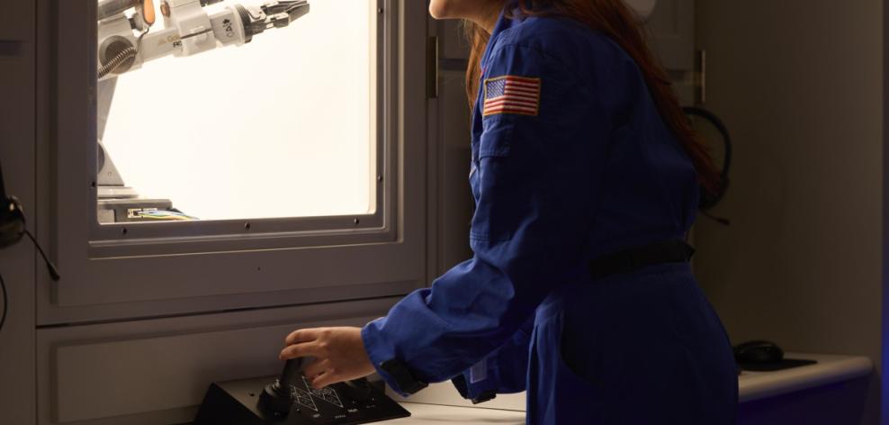 A teenage student participates in a space mission simulation at the McAuliffe Center’s Challenger Learning Center. The student is looking out the window of a room designed to look like the inside of a space shuttle, wearing a blue uniform with an American flag patch.